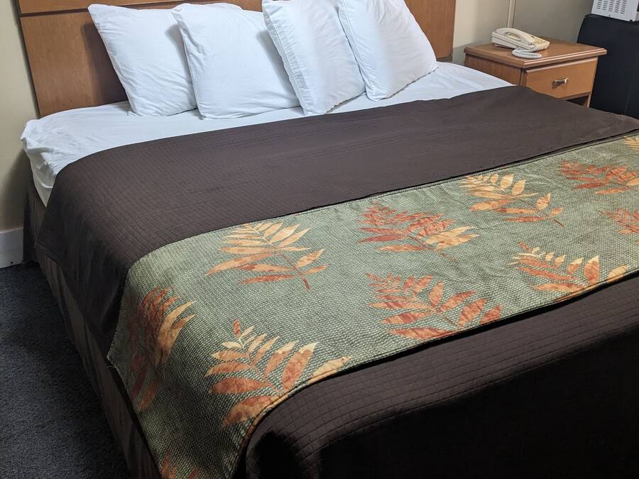 Una cama bien hecha con un edredón marrón y una manta estampada con motivos florales.