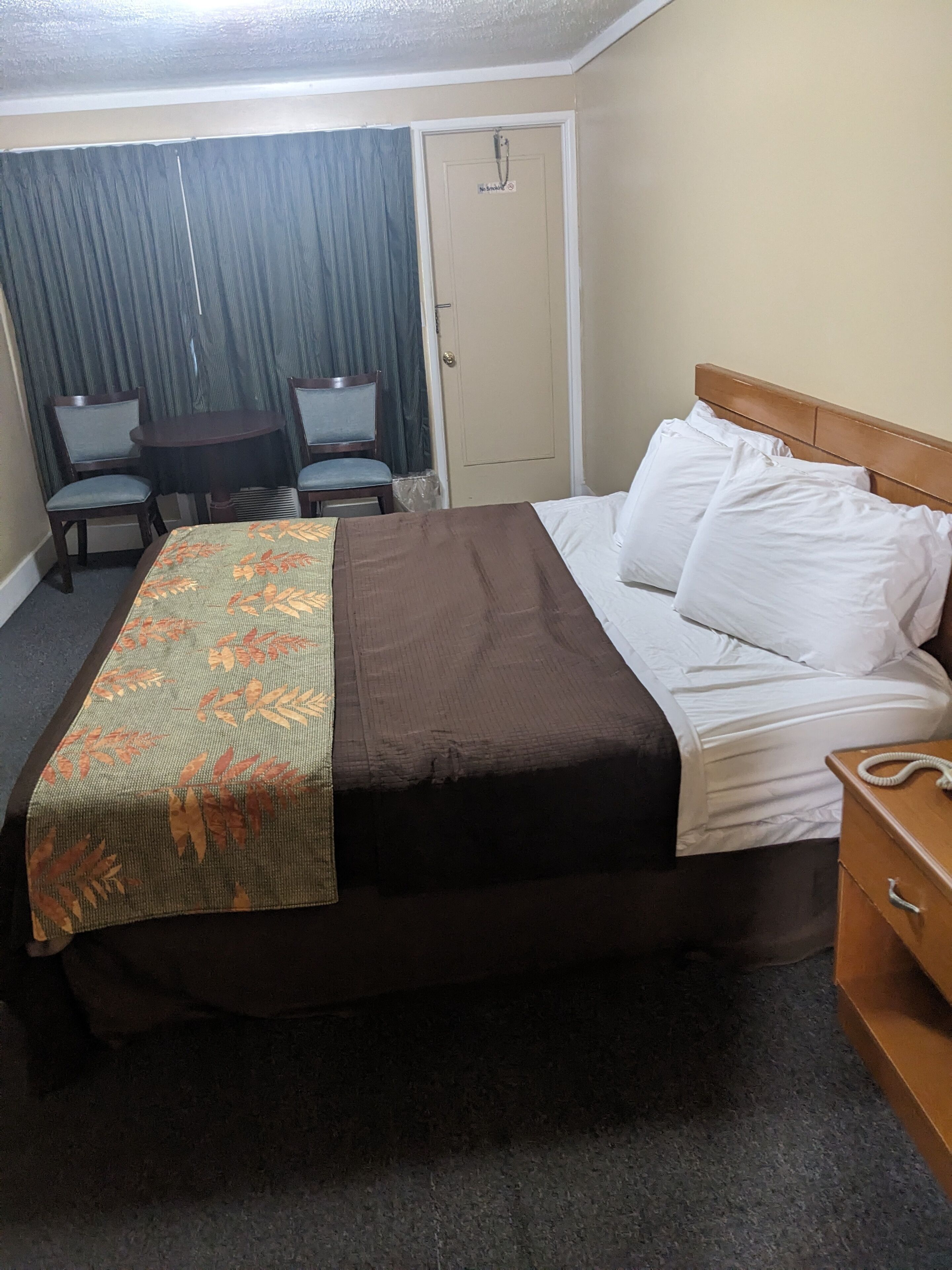 A hotel room with a bed, a bedside table, a chair, a small table, and a door.