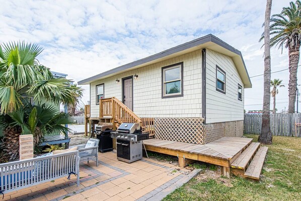 A single-story house with a deck, a barbecue grill, and a wooden staircase. - Angler's Court (Port Aransas)