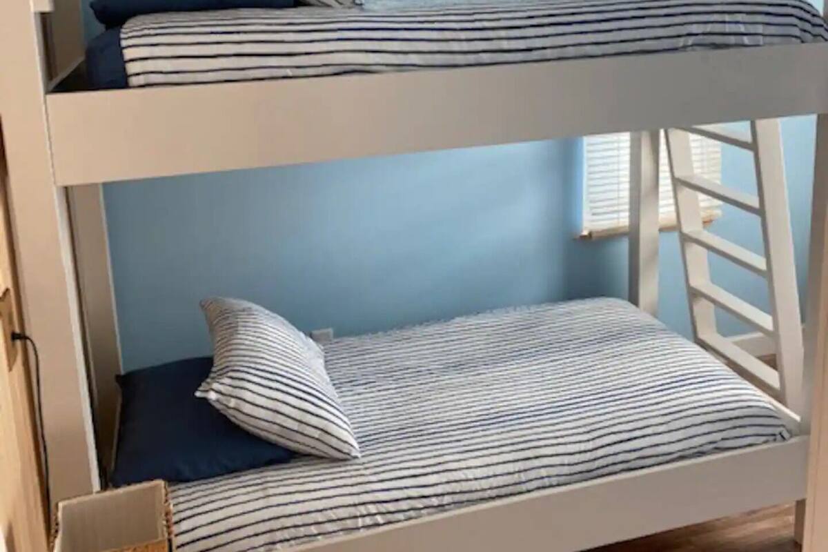 Ein Stockbett mit gestreifter Bettwäsche in einem Zimmer mit blauen Wänden und Holzboden.