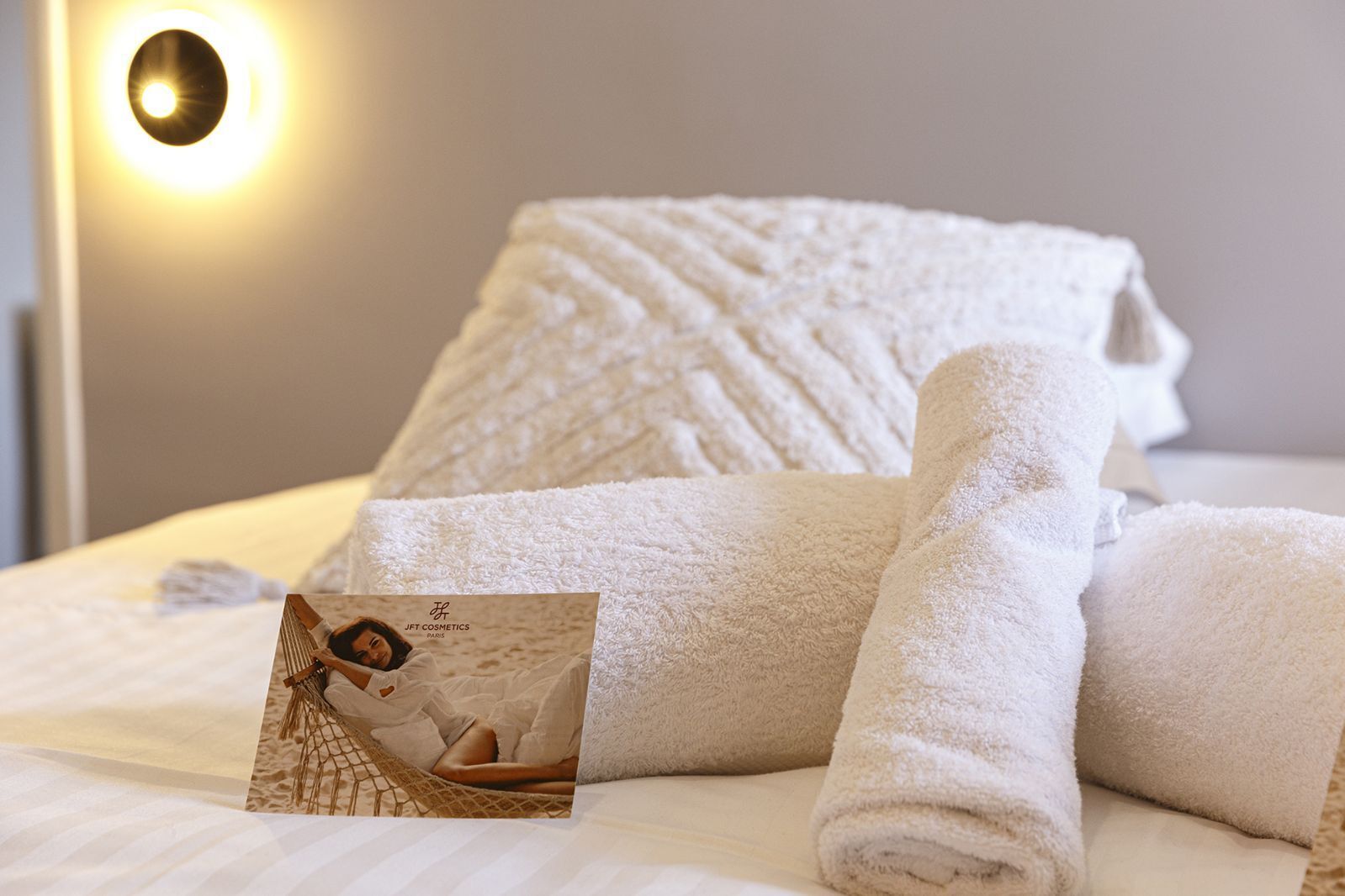Un lit bien fait, avec des serviettes blanches pliées en rouleau et une brochure posée dessus.
