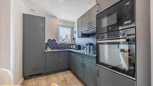 A modern kitchen with grey cabinets, a built-in oven, and a window overlooking the city. - L'hermès, Douillet et Chaleureux, Venez Vous Détendre (Segré-en-Anjou Bleu)