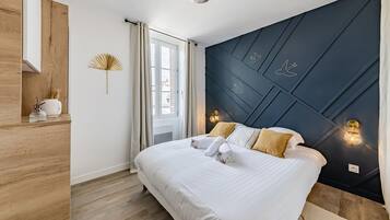 Ein modernes Schlafzimmer mit einem großen Bett, Holzboden, einer dunklen Wand mit Vogelmotiven und einem Fenster mit Vorhängen.