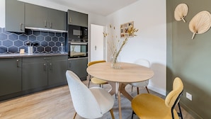 A modern kitchen with dark cabinets, a microwave, and an oven. There is a dining table with chairs and a vase with dried plants. - L'hermès, Douillet et Chaleureux, Venez Vous Détendre (Segré-en-Anjou Bleu)