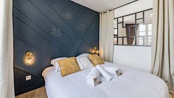Een hotelkamer met een bed, twee kussens, een nachtkastje, een spiegel en een raam met gordijnen.
