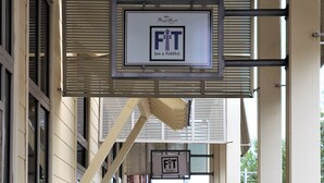 Un pasillo de madera que conduce a un edificio con un letrero que dice "FIT Too!" y otro anuncio que ofrece "ONE ONCE Entrenamiento Disponible Ya."
