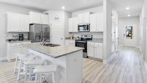 Una cocina moderna con armarios blancos, encimera de granito, electrodomésticos de acero inoxidable y una isla central con taburetes de bar.