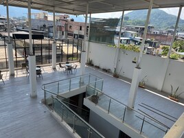 Una amplia terraza en la azotea con barandilla de vidrio, mobiliario exterior y plantas en macetas.