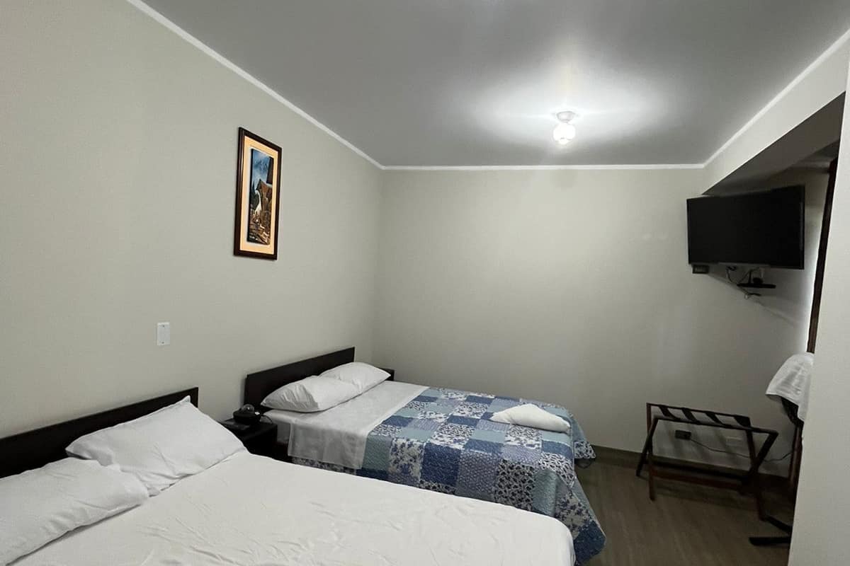 A hotel room with two beds, a flat-screen TV mounted on the wall, and a ceiling light.