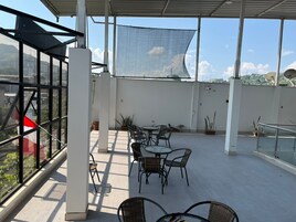 Una terraza en la azotea con una mesa, sillas, plantas en macetas y vistas panorámicas de la ciudad.