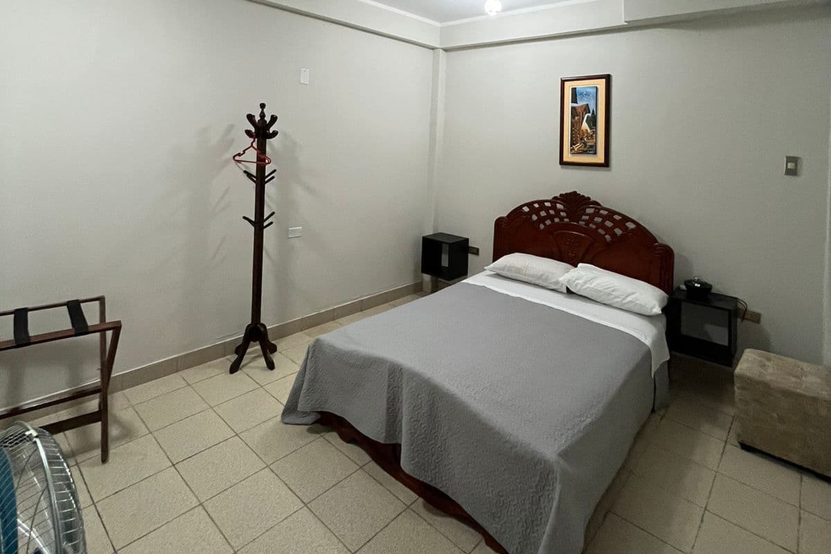 A bedroom with a bed, a ceiling fan, a nightstand, a framed picture on the wall, and a coat rack.