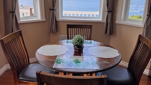 En matplats med ett runt bord, fyra stolar och utsikt över havet och bergen genom stora fönster.