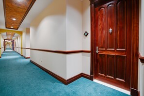 A hotel hallway with a blue carpet, wooden wainscoting, and a large wooden door with a brass handle.