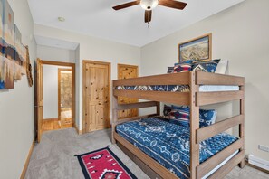 A bunk bed with a patterned bedspread, a ceiling fan, and a door leading to a bathroom. - Modern luxury condo for your Angel Fire stay (Angel Fire)