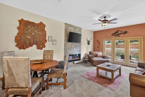 A living room with a fireplace, a ceiling fan, and a large wall-mounted TV.