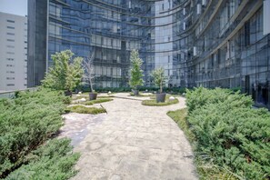 A modern building with a curved glass facade, a paved courtyard with potted plants, and a clear pathway.
