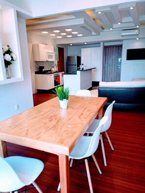 Een moderne keuken met witte kasten, een magnetron en een eethoek met een houten tafel en witte stoelen.