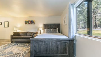 A bedroom with a wooden headboard, a large window with a view of trees, a sofa, and a patterned rug.