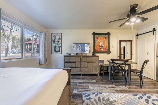 A bedroom with a bed, a desk, a chair, a television, and artwork on the walls.