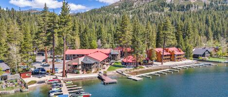 A lakeside lodge with multiple buildings, docked boats, and a forested mountain backdrop.