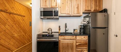 A compact kitchen with wooden cabinets, stainless steel appliances, and a built-in microwave.