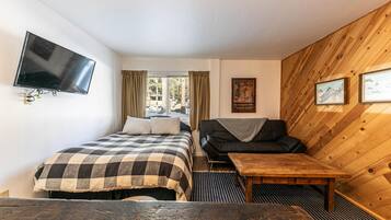 A room with a bed, a sofa, a TV, a wooden wall, and a window.