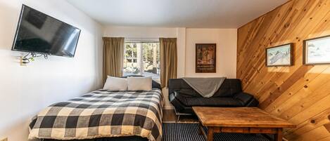 Quarto com cama, sofá, televisão, parede de madeira e janela.