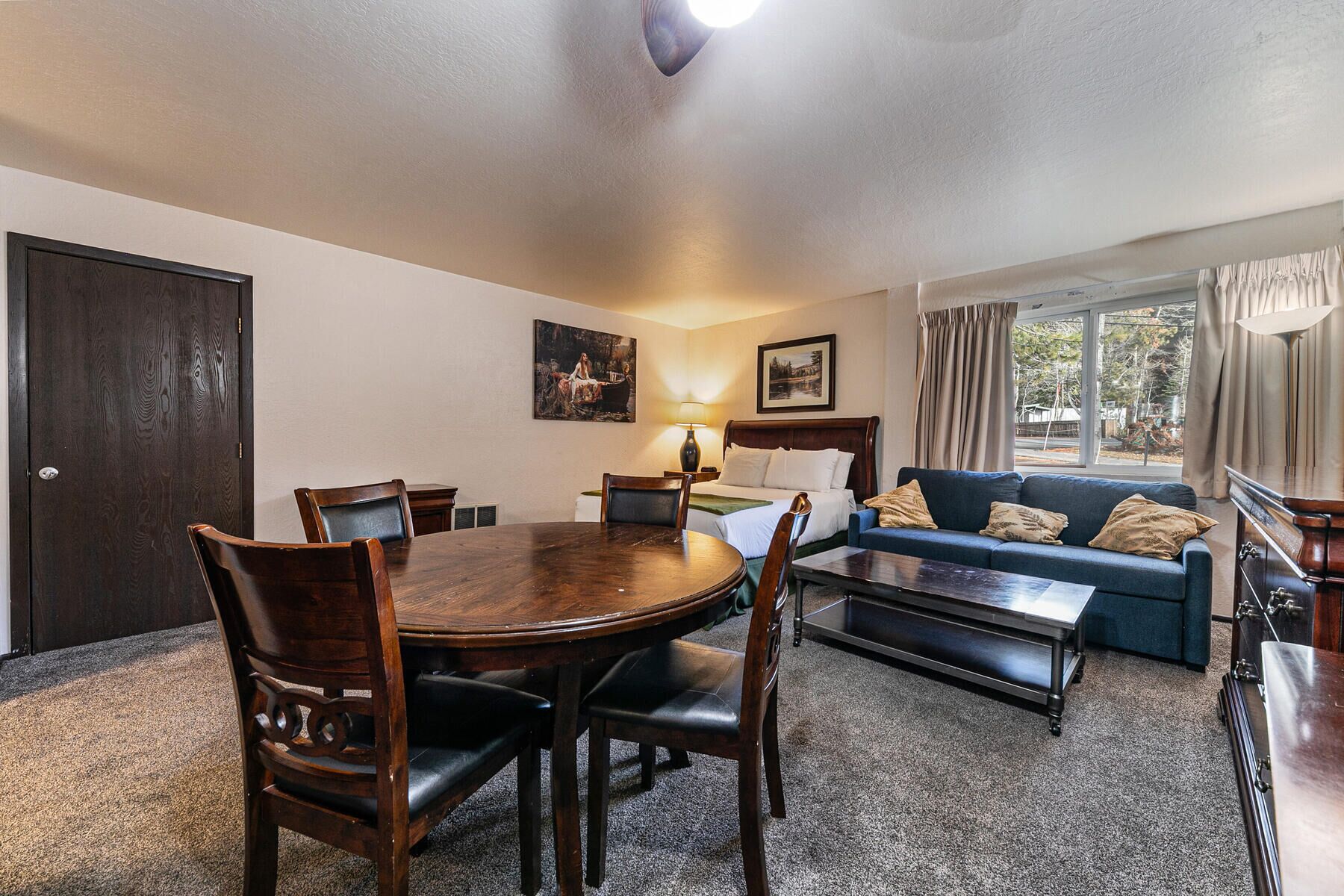 Quarto de hotel com mesa de jantar, cadeiras, sofá, cama e janela com cortinas.