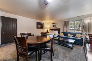 Una habitación de hotel con una mesa de comedor, sillas, un sofá, una cama y una ventana con cortinas.