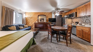 Een compacte hotelkamer met een bank, een eettafel met stoelen, een kitchenette en een plafondventilator.