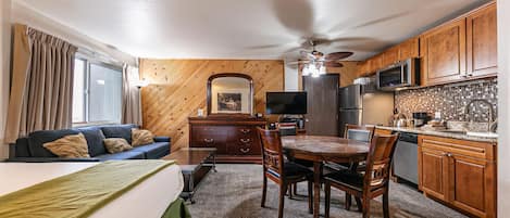 Ein kompaktes Hotelzimmer mit Sofa, Esstisch mit Stühlen, einer Küchenzeile und Deckenventilator.