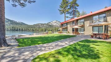 A lakeside hotel with a well-maintained lawn, outdoor seating, and a view of the lake and mountains.