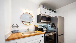 A modern kitchen with white cabinets, a wooden countertop, stainless steel appliances, and a round mirror above the sink. - Striking Deluxe Studio w/Kitchen #114 at Donner Lake Village (Truckee)