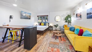 A modern, well-lit room with a bed, a yellow sofa, a dining table, and a small round table. - Striking Deluxe Studio w/Kitchen #114 at Donner Lake Village (Truckee)