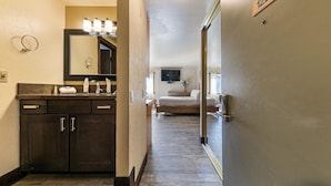 Une chambre d’hôtel avec une coiffeuse en bois foncé, un grand miroir et un lit surmonté d’un téléviseur.