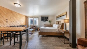 Une chambre d’hôtel avec un plafond en bois, un lit, un bureau, une chaise, une télévision et une fenêtre avec des rideaux.