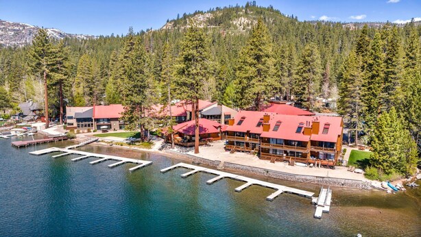 A lakeside lodge with multiple buildings, docked boats, and a mountainous backdrop.