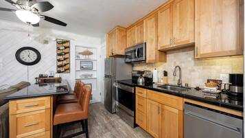A modern kitchen with wooden cabinets, stainless steel appliances, a black countertop, and a ceiling fan.