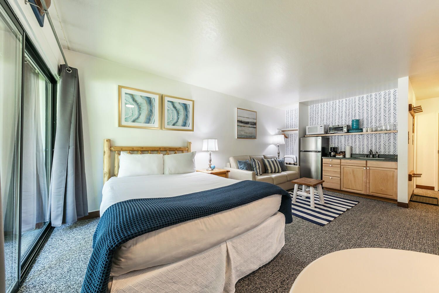 A hotel room with a bed, a sofa, a small table, a kitchenette, and a window with curtains.