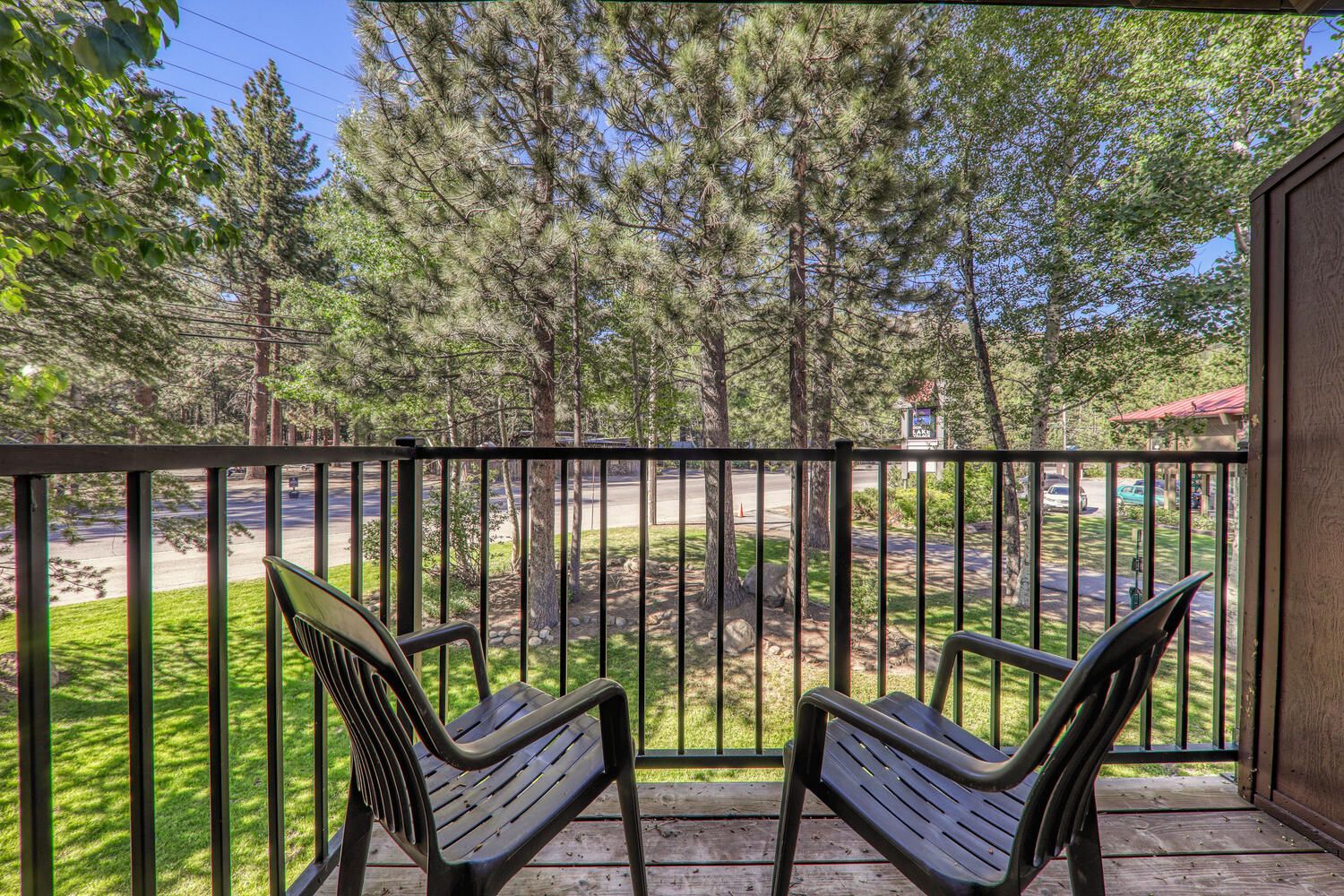 A balcony with two chairs, a wooden deck, and a view of a road and trees.