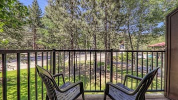 A balcony with two chairs, a wooden deck, and a view of a road and trees.