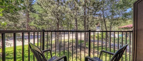 A balcony with two chairs, a wooden deck, and a view of a road and trees.