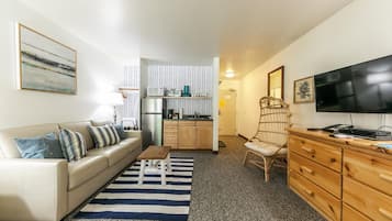 Ett kompakt bostadsutrymme med en soffa, ett litet bord, en köksdel och en tv.