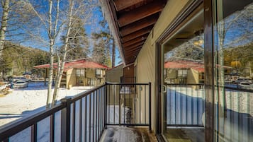 A balcony with a wooden railing, a glass door, and a view of a snowy landscape with trees and parked cars.