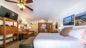 A hotel room with a bed, a wooden dresser, a desk, a chair, a sofa, a ceiling fan, a kitchen area, and artwork on the walls. - Cozy Studio w/Kitchenette and Balcony #212 at Donner Lake Village (Truckee)