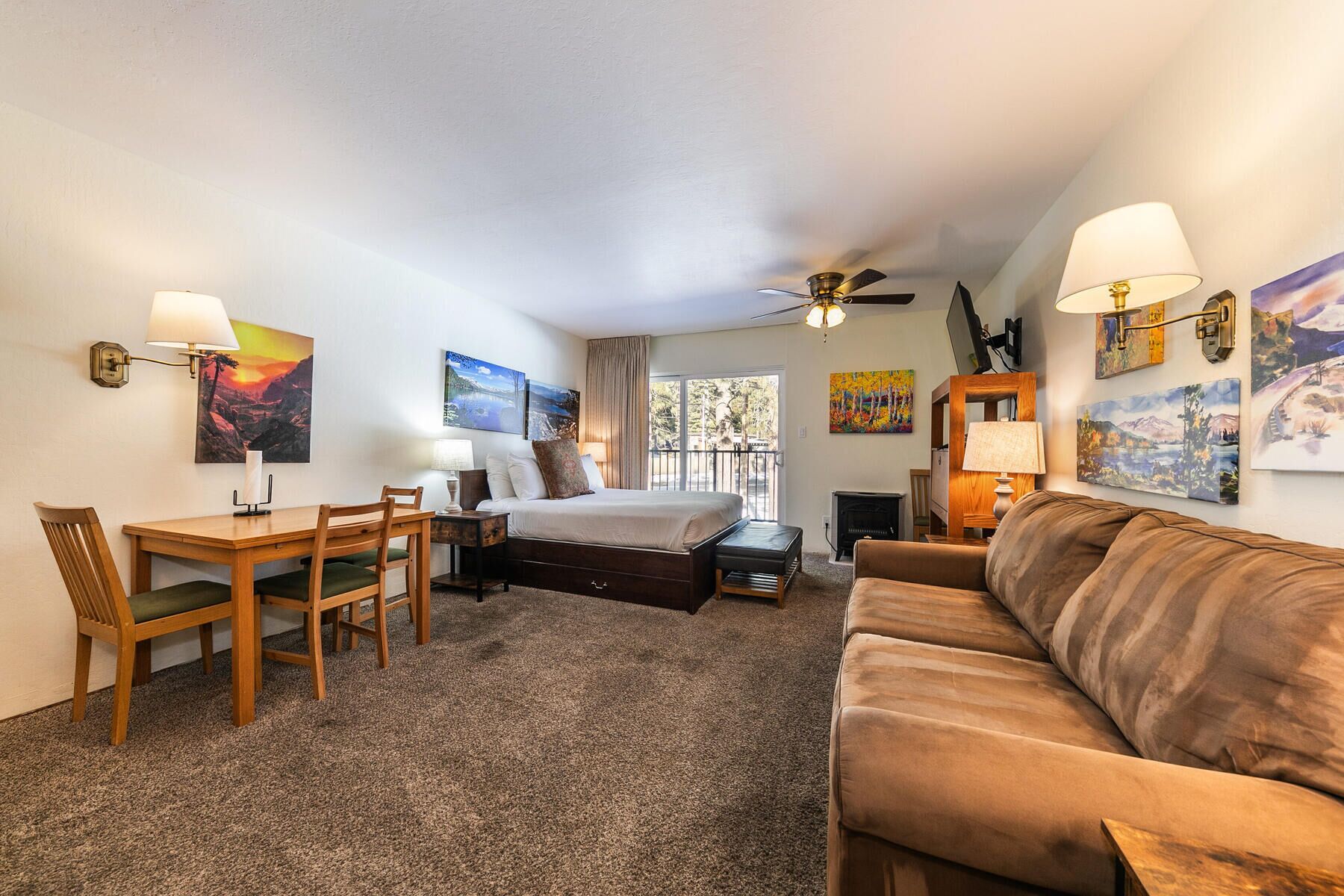 A hotel room with a bed, a sofa, a dining table with chairs, and artwork on the walls.