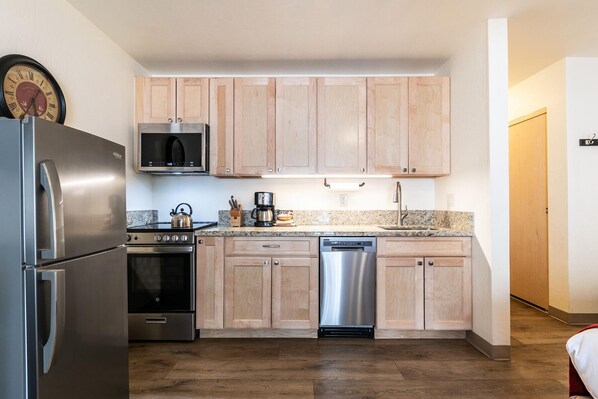 Une cuisine compacte dotée de meubles en bois, d’appareils électroménagers en acier inoxydable, d’un four à micro-ondes, d’une bouilloire et d’une machine à café.
