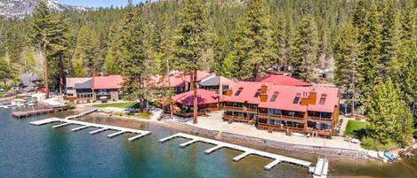 A lakeside lodge with multiple buildings, docked boats, and a mountainous backdrop.
