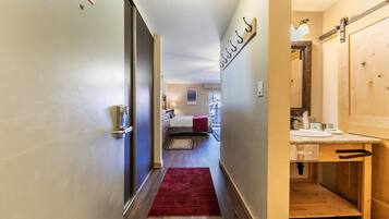 A hotel hallway with a bed, a red rug, and a wooden door.