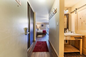 Un couloir d’hôtel avec un lit, un tapis rouge et une porte en bois.